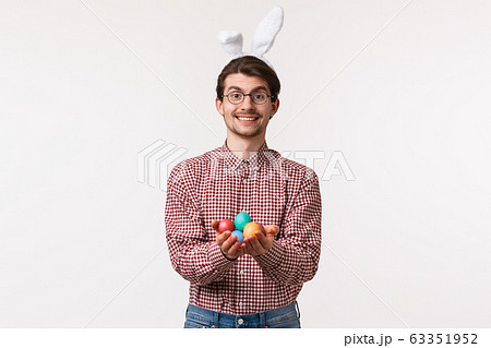 Traditions, religious holidays, celebration concept. Lovely and caring adult man in glasses and rabbit ears, holding painted eggs and smiling, give it to person and congratulate with happy Easter day 63351952