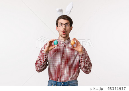 Traditions, religious holidays, celebration concept. Amused enthusiastic handsome young man suggest girlfriend play Easter game on family gathering party, hold two painted eggs, wear rabbit ears Traditions, religious holidays, celebration concept. Amused enthusiastic handsome young man suggest girlfriend play Easter game on family gathering party, hold two painted eggs, wear rabbit ears 63351957