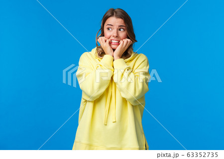 Scared timid, insecure european female feeling panic and afraid staying alone at home, biting fingernails look away as trembling fear, standing unsafe place over blue background 63352735
