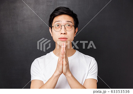 Close-up portrait of hopeful dreamy young asian guy in glasses and white t-shirt, hold hands together in pray, looking up pleading, anticipating miracle, awaiting results with hope 63353536