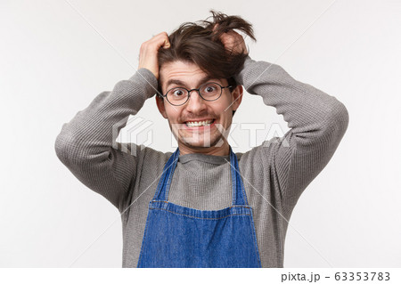 Portrait of distressed and tensed young male barista going insane with lots orders, pulling hair out of head crazy look camera, cant bear stress, feeling disturbed and annoyed, white background 63353783