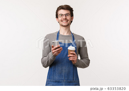 Portrait of cheerful young male employee suggest to use promo code with mobile phone app to receive discount at his coffee shop, holding take-away cup and smartphone smiling camera 63353820
