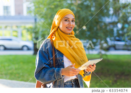 Arab woman student. Beautiful muslim female student wearing bright yellow hijab holding tablet. Arab woman student. Beautiful muslim female student wearing bright yellow hijab holding tablet. 63354074