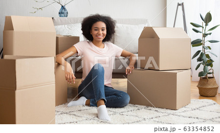 Smiling african american girl sitting on floor surrounded by a lot of boxes Smiling african american girl sitting on floor surrounded by a lot of boxes 63354852