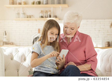 Mature woman playing video games on smartphone with her granddaughter at home 63354854