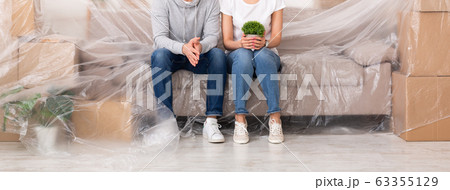Unrecognizable couple sitting on covered sofa while moving in new flat Unrecognizable couple sitting on covered sofa while moving in new flat 63355129