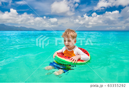 Toddler boy on beach swimming with inflatable ring 63355292