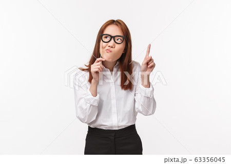 Holidays, office life and women concept. Portrait of thoughtful funny asian female entrepreneur holding glasses on stick mask and pouting while thinking, look away raise finger on eureka gesture 63356045