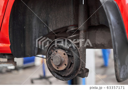 Rusty drum brakes, rear on red car. Change the old to new brake disc on car in a garage. Auto mechanic repairing Rusty drum brakes, rear on red car. Change the old to new brake disc on car in a garage. Auto mechanic repairing 63357171