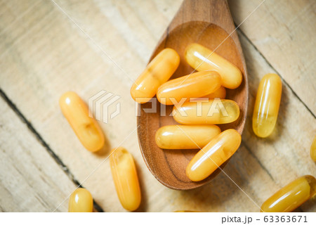 Royal jelly capsules in wooden spoon and wood 63363671