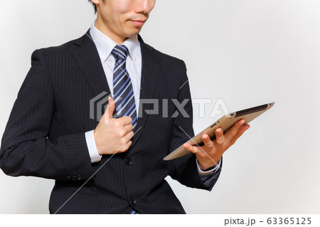 タブレットを持って親指を立てるスーツ姿の男性 63365125