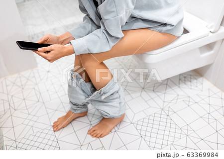 Woman with phone on the toilet bowl 63369984