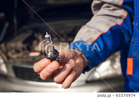 Car service men. Replacing a burnt out lamp in the car headlight Car service men. Replacing a burnt out lamp in the car headlight 63370974