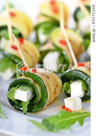 Delicious rolls of fried zucchini slices and feta cheese with rucola, served with olive oil and pieces of bell peppers Delicious rolls of fried zucchini slices and feta cheese with rucola, served with olive oil and pieces of bell peppers 63371144