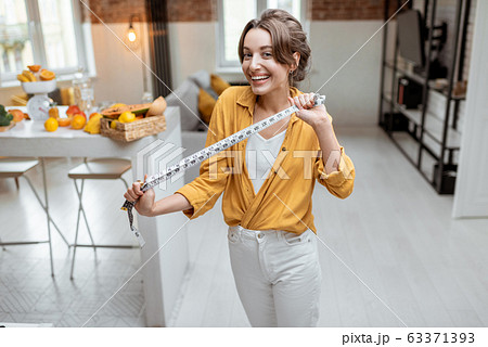 Cheerful woman with measuring tape at home Cheerful woman with measuring tape at home 63371393