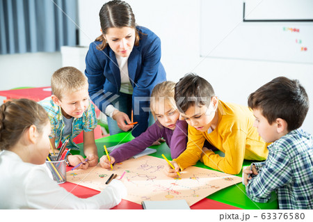 Teacher and happy schoolkids playing board game 63376580