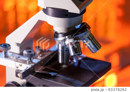 Close up of microscope lenses focused on a specimen in warm orange light light. Close up of microscope lenses focused on a specimen in warm orange light light. 63378262