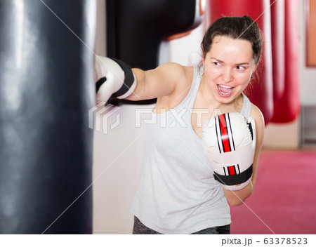 Enthusiastic sportswoman in the boxing hall practicing boxing punches with boxing bag Enthusiastic sportswoman in the boxing hall practicing boxing punches with boxing bag 63378523