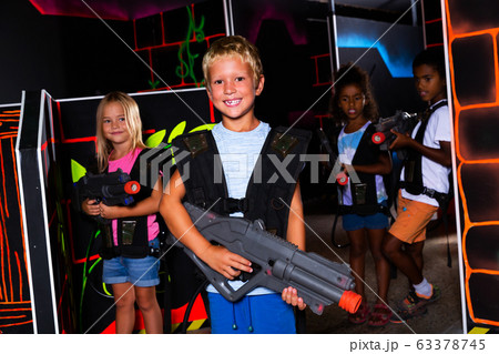 Positive teen boy standing with laser pistol in dark lasertag room during game with friends Positive teen boy standing with laser pistol in dark lasertag room during game with friends 63378745