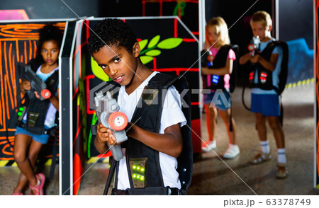 Emotional afro-american boy with laser pistol playing laser tag with friends on dark labyrinth 63378749