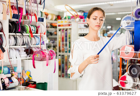 Interested young woman choosing colorful ribbons and braid for dressmaking in sewing supplies shop Interested young woman choosing colorful ribbons and braid for dressmaking in sewing supplies shop 63379627
