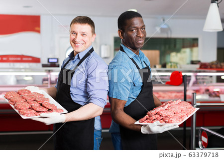 professional butchers standing in butcher shop with trays 63379718