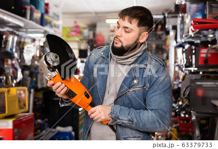 Adult bearded man is looking on new angle grinder in tools store 63379733