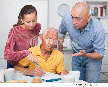 Adult children help an older father sign documents 63380557