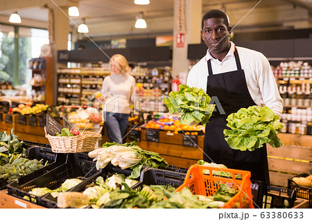 Grocery worker arranging vegetables on counter Grocery worker arranging vegetables on counter 63380633