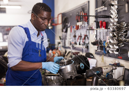 Afro american worker in overalls inspects a motorcycle engine 63380697