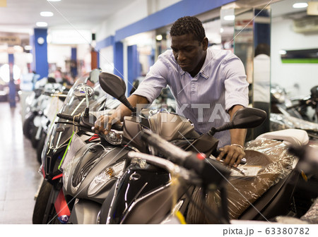 Afro american man is shopping and choosing new motobike in moto store Afro american man is shopping and choosing new motobike in moto store 63380782