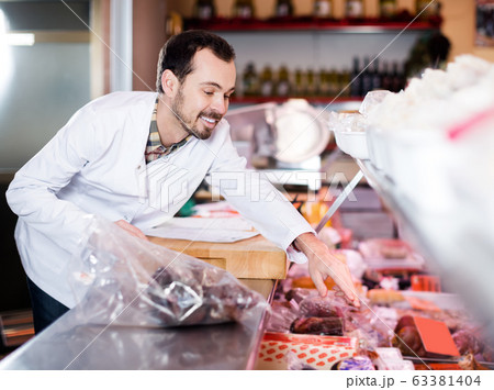 Smiling male seller showing tasty sausages Smiling male seller showing tasty sausages 63381404