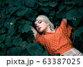 Beautiful woman lying among darkgreen plants, pretty girl relaxing outdoor. Close-up 63387025