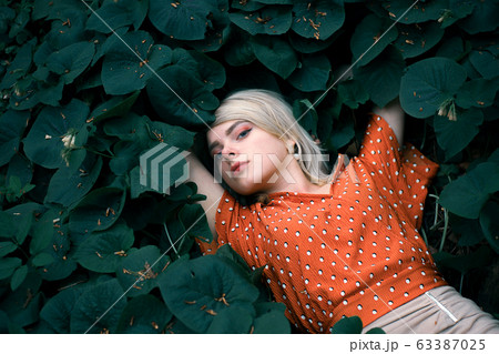 Beautiful woman lying among darkgreen plants, pretty girl relaxing outdoor. Close-up 63387025