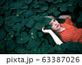 Beautiful woman lying among darkgreen plants, pretty girl relaxing outdoor. Close-up 63387026