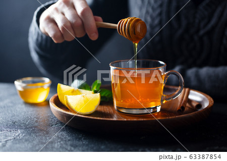 Cup of tea with pouring honey and lemon. Grey background. Cup of tea with pouring honey and lemon. Grey background. 63387854
