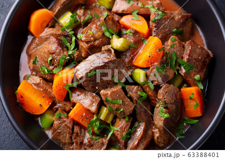 Beef meat and vegetables stew in black bowl. Dark background. Close up. Beef meat and vegetables stew in black bowl. Dark background. Close up. 63388401
