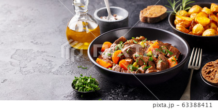 Beef meat and vegetables stew in black bowl with roasted baby potatoes. Dark background. Copy space. Beef meat and vegetables stew in black bowl with roasted baby potatoes. Dark background. Copy space. 63388411