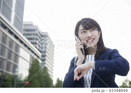 屋外で電話をかけながら腕時計を見る丸の内OL 63398699