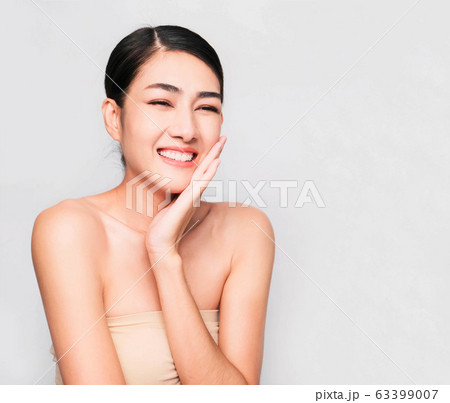 young beautiful asian woman with clean and bright skin, Cosmetic Beauty Concept,hands touch on the cheek, smiling and friendly face isolated on grey background 63399007