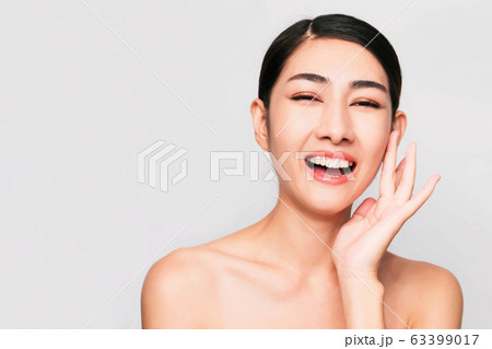 young beautiful asian woman with clean and bright skin, Cosmetic Beauty Concept,hands touch on the cheek, smiling and friendly face isolated on grey background 63399017