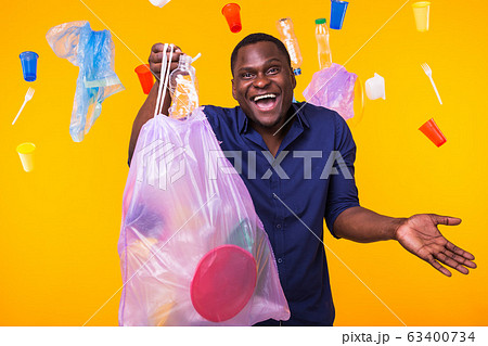 Problem of trash, plastic recycling, pollution and environmental concept - funny man carrying garbage bag on yellow background Problem of trash, plastic recycling, pollution and environmental concept - funny man carrying garbage bag on yellow background 63400734