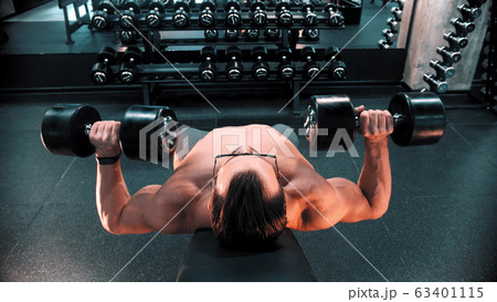 A man bodybuilder in glasses pumping his hands muscles lying on the stand in the gym 63401115