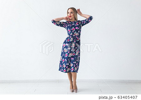 Fashionable young blonde woman in beautiful summer dress posing at white studio with copy space. Fashionable young blonde woman in beautiful summer dress posing at white studio with copy space. 63405407