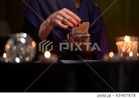 Fortuneteller female divines on cards at table with candles Fortuneteller female divines on cards at table with candles 63407878