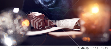 Close-up of fortune-teller's hands, book of predictions, burning candle 63407939