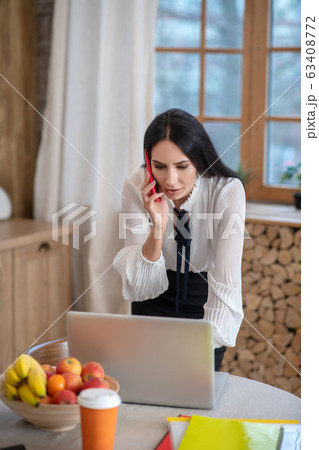 Young woman checking something on laptop, talking on phone Young woman checking something on laptop, talking on phone 63408772