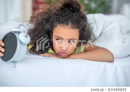 Awakened girl with brown eyes looking at the alarm clock. Awakened girl with brown eyes looking at the alarm clock. 63408895