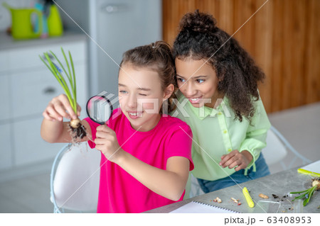 Sitting next to two girls, looking at the roots. 63408953