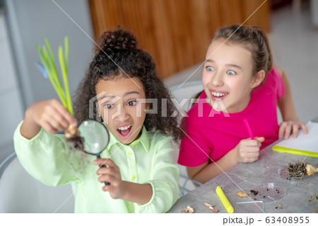 Two teenage girls looking in surprise at the root of plant. Two teenage girls looking in surprise at the root of plant. 63408955